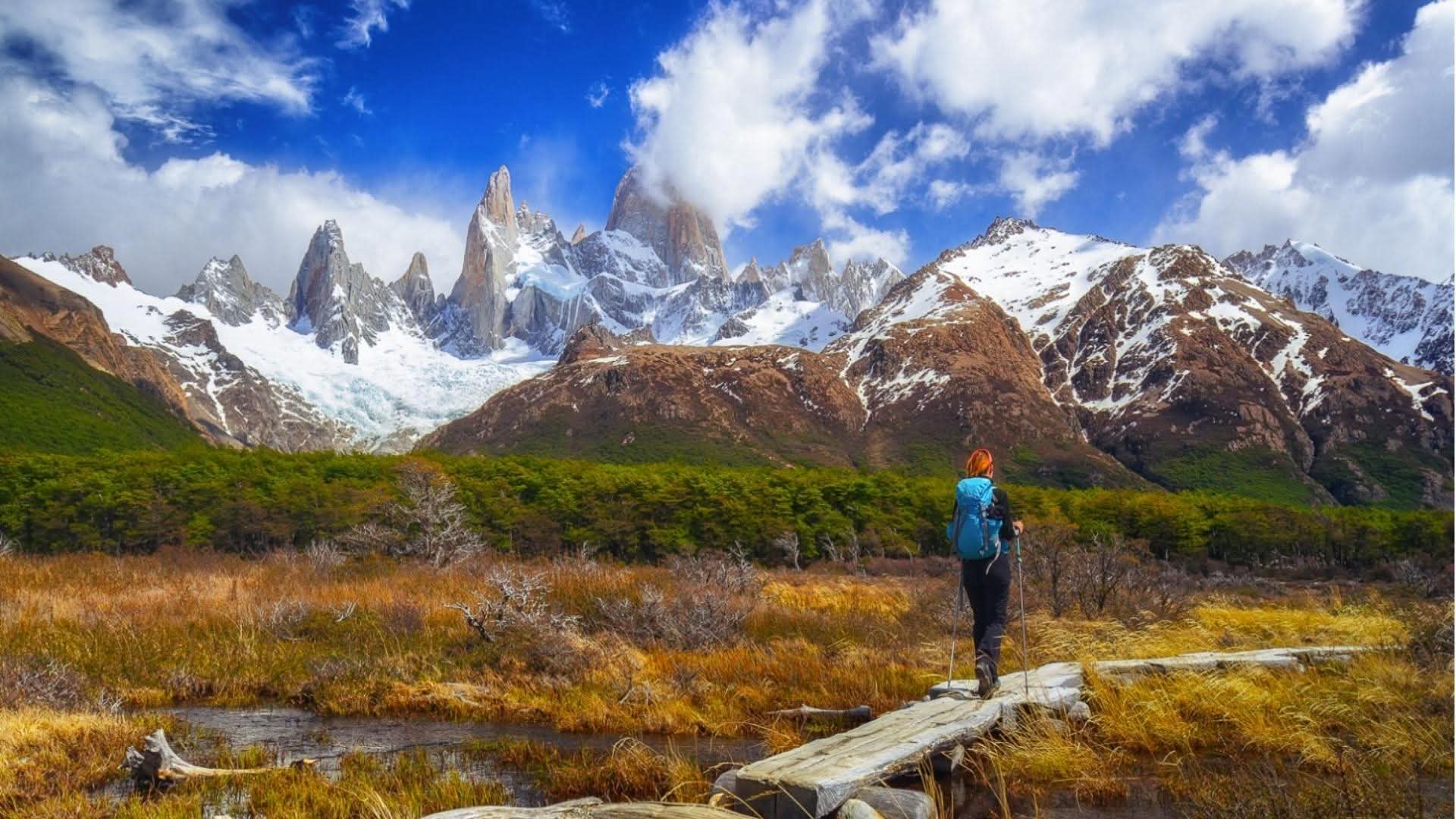 Solo hiker admiring the snow-covered peaks of Patagonia, Argentina, while trekking through a remote mountain landscape under a clear blue sky.